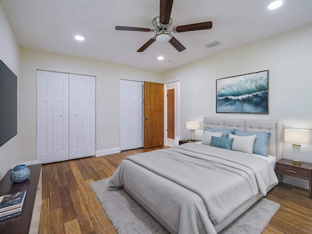 bedroom featuring dark hardwood / wood-style flooring, ceiling fan, and multiple closets