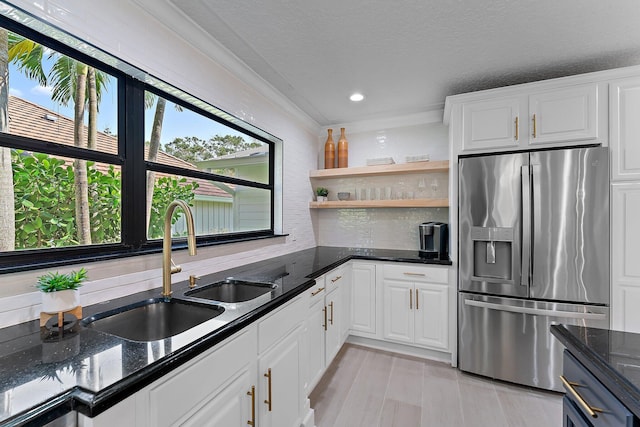 kitchen with stainless steel refrigerator with ice dispenser, sink, white cabinetry, crown molding, and dark stone countertops