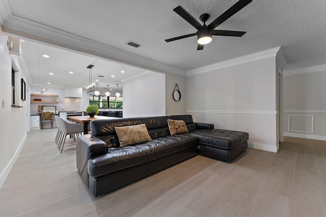 living room featuring ceiling fan, ornamental molding, light hardwood / wood-style flooring, and a textured ceiling