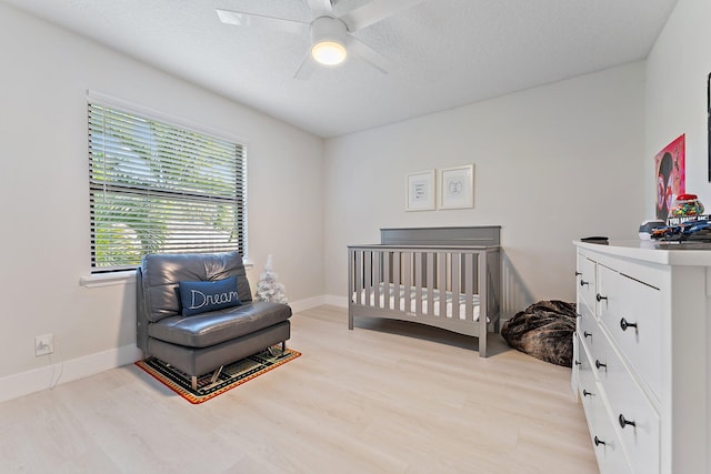 bedroom featuring ceiling fan, light hardwood / wood-style flooring, a crib, and a textured ceiling