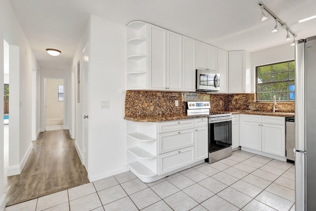 kitchen with white cabinetry, appliances with stainless steel finishes, backsplash, and dark stone countertops