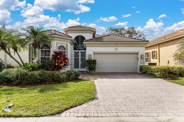 mediterranean / spanish home with a garage, a tiled roof, decorative driveway, a front lawn, and stucco siding