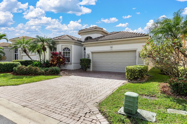 mediterranean / spanish house featuring a garage, decorative driveway, a tile roof, and stucco siding