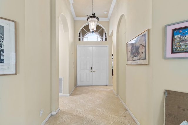 entrance foyer with a notable chandelier, crown molding, baseboards, and light tile patterned floors