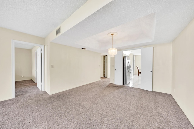 carpeted empty room featuring a raised ceiling, an inviting chandelier, and a textured ceiling