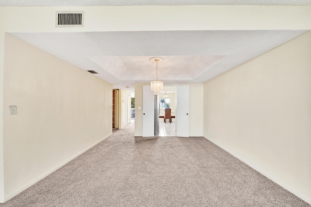 carpeted empty room with a tray ceiling, a textured ceiling, and a notable chandelier