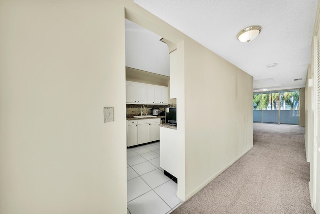 corridor featuring sink, a textured ceiling, and light tile patterned floors