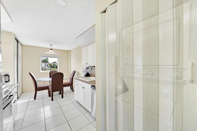 kitchen with pendant lighting, sink, white cabinets, light tile patterned floors, and a textured ceiling