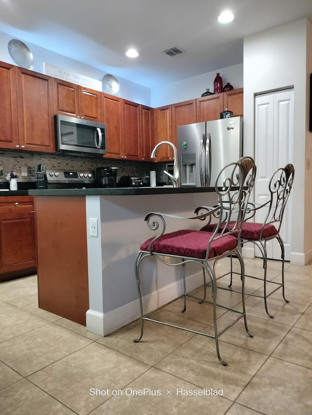 kitchen featuring light tile patterned floors, decorative backsplash, stainless steel appliances, and a kitchen breakfast bar