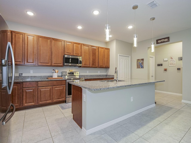 kitchen featuring sink, hanging light fixtures, stainless steel appliances, light stone counters, and a center island with sink