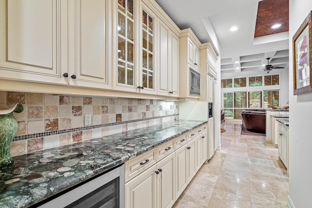 kitchen featuring coffered ceiling, tasteful backsplash, dark stone countertops, ceiling fan, and cream cabinets