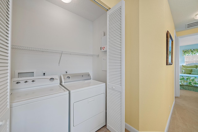 laundry area with light colored carpet, washing machine and dryer, and a textured ceiling