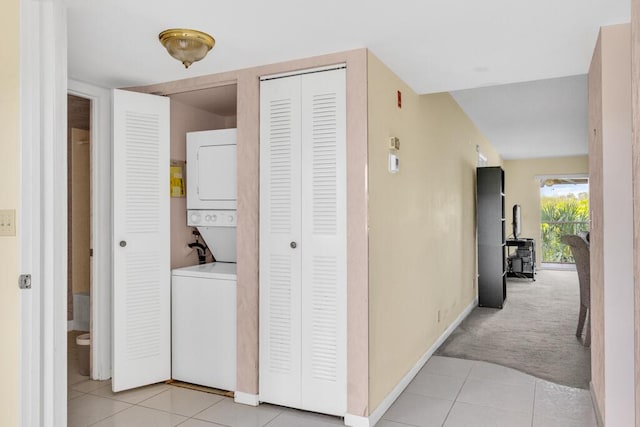 hallway with light tile patterned floors, stacked washer and dryer, light colored carpet, and baseboards