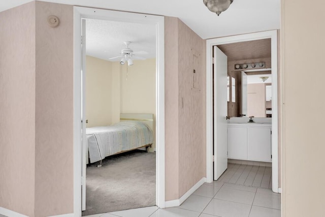 corridor with baseboards, light tile patterned flooring, a sink, and light colored carpet