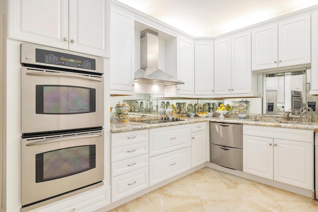 kitchen with black electric stovetop, double oven, white cabinetry, light stone countertops, and wall chimney exhaust hood