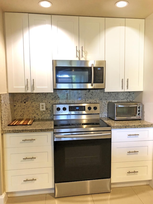 kitchen featuring light tile patterned floors, white cabinetry, dark stone countertops, stainless steel appliances, and decorative backsplash