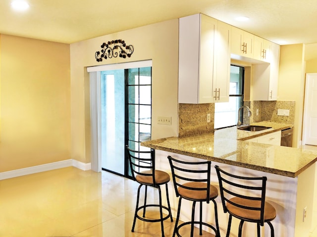 kitchen featuring sink, a kitchen bar, white cabinets, stone countertops, and kitchen peninsula