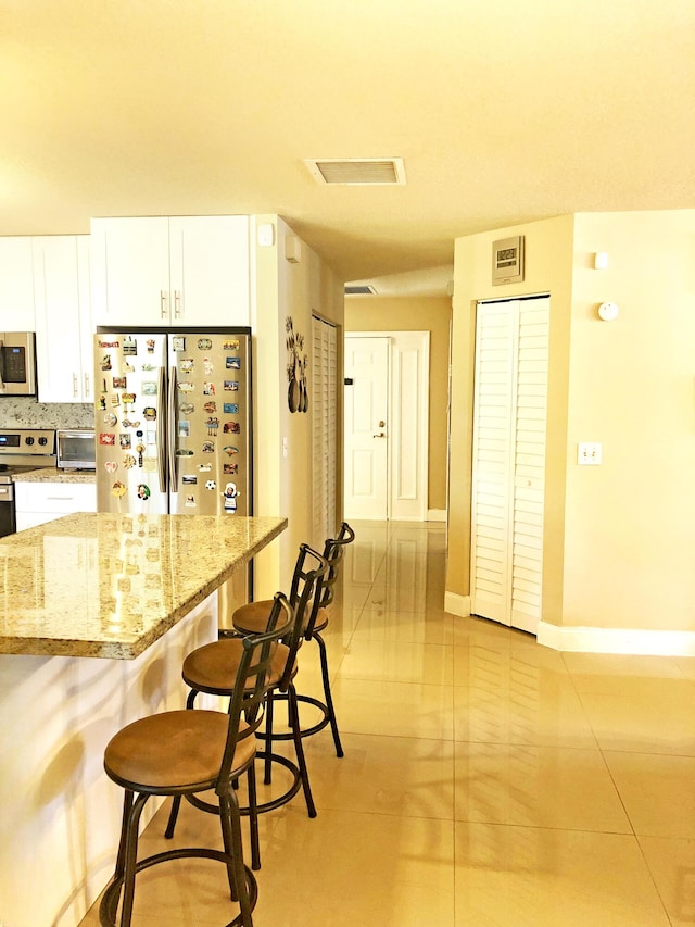 kitchen with tasteful backsplash, white cabinetry, a kitchen breakfast bar, stainless steel appliances, and light stone countertops