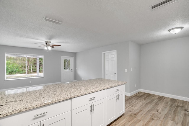 kitchen featuring light wood-type flooring, a textured ceiling, white cabinets, and light stone counters