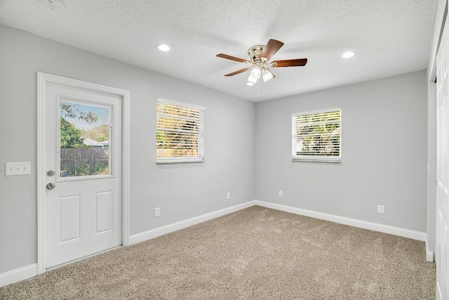 empty room featuring ceiling fan, a wealth of natural light, a textured ceiling, and carpet flooring