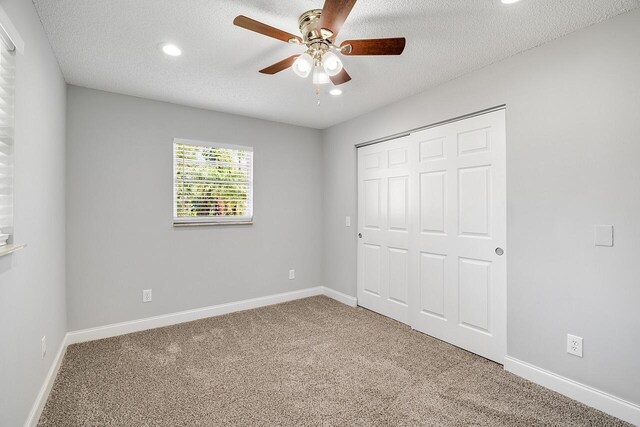 unfurnished bedroom featuring ceiling fan, a closet, a textured ceiling, and carpet