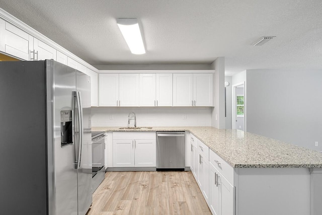 kitchen with sink, light stone counters, kitchen peninsula, stainless steel appliances, and white cabinets