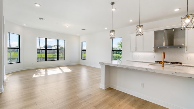 kitchen featuring white cabinetry, light stone counters, decorative light fixtures, wall chimney range hood, and backsplash