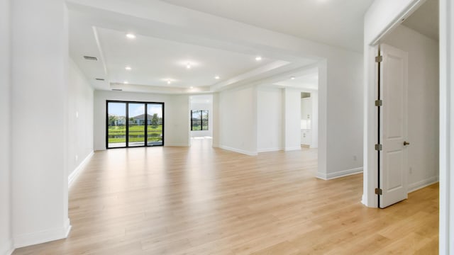 unfurnished living room with a tray ceiling and light wood-type flooring