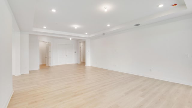 spare room with a tray ceiling and light hardwood / wood-style floors