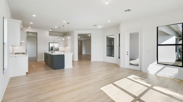 kitchen with decorative light fixtures, a center island with sink, stainless steel fridge, light hardwood / wood-style floors, and white cabinets