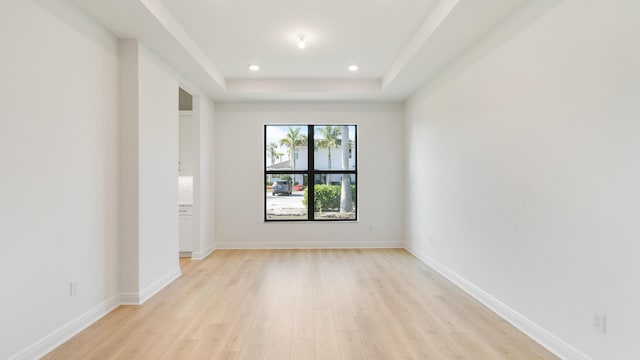 spare room featuring a tray ceiling and light hardwood / wood-style flooring