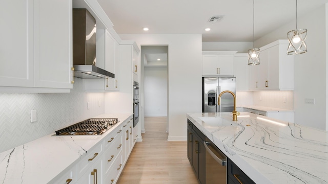 kitchen with wall chimney exhaust hood, decorative light fixtures, stainless steel appliances, light stone countertops, and white cabinets