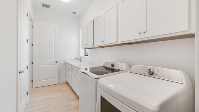 laundry area with cabinets, washer and clothes dryer, sink, and light wood-type flooring