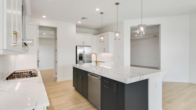 kitchen with appliances with stainless steel finishes, decorative light fixtures, an island with sink, white cabinets, and light hardwood / wood-style flooring