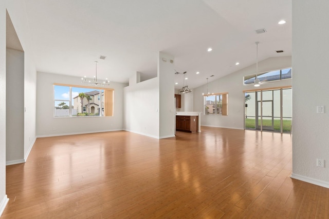 unfurnished living room with high vaulted ceiling, ceiling fan with notable chandelier, and light hardwood / wood-style floors