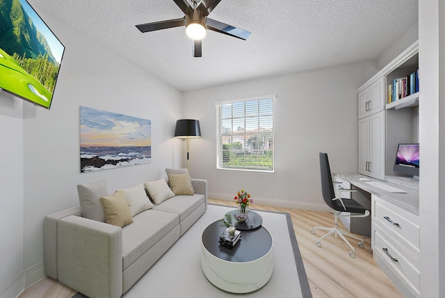 home office with a ceiling fan, baseboards, built in desk, a textured ceiling, and light wood-type flooring