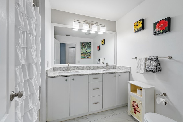 bathroom featuring a sink, toilet, marble finish floor, and double vanity