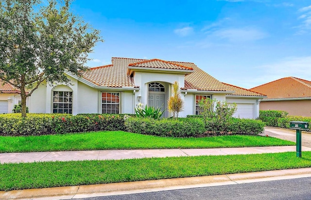 mediterranean / spanish home featuring stucco siding, an attached garage, a tile roof, and a front yard