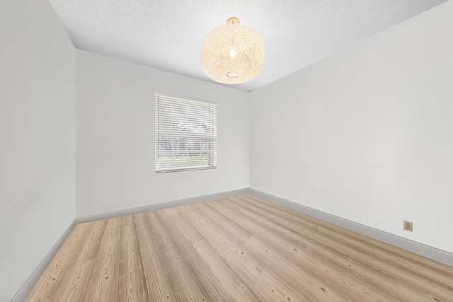 empty room with baseboards, a textured ceiling, and light wood finished floors