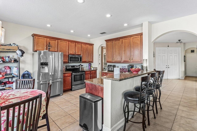 kitchen featuring light tile patterned floors, dark stone countertops, stainless steel appliances, a kitchen breakfast bar, and a textured ceiling