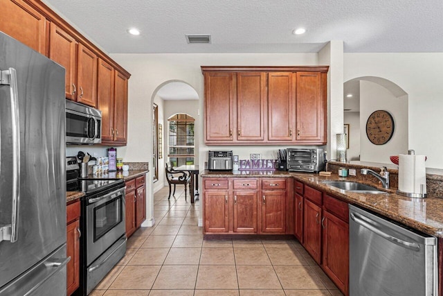 kitchen featuring sink, light tile patterned flooring, dark stone counters, and appliances with stainless steel finishes