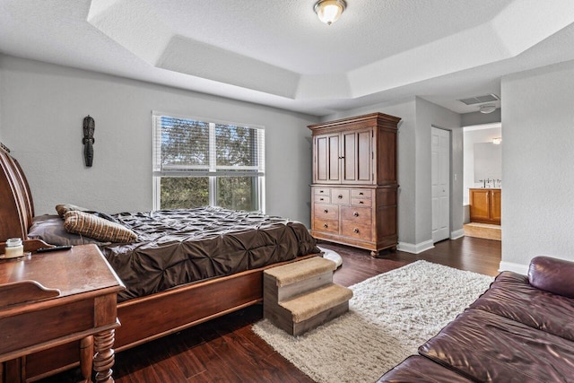 bedroom with a tray ceiling, dark wood-type flooring, ensuite bath, and a textured ceiling