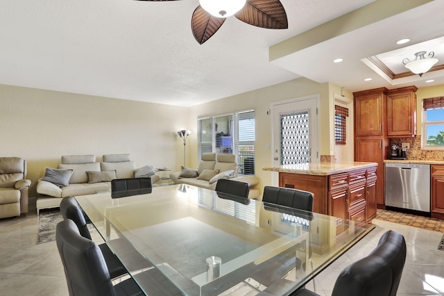 tiled dining space with ceiling fan and a tray ceiling