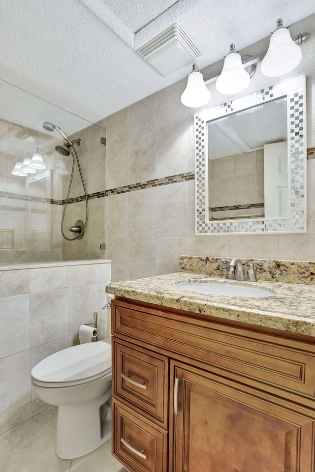 bathroom featuring tile walls, tile patterned flooring, vanity, tiled shower, and toilet