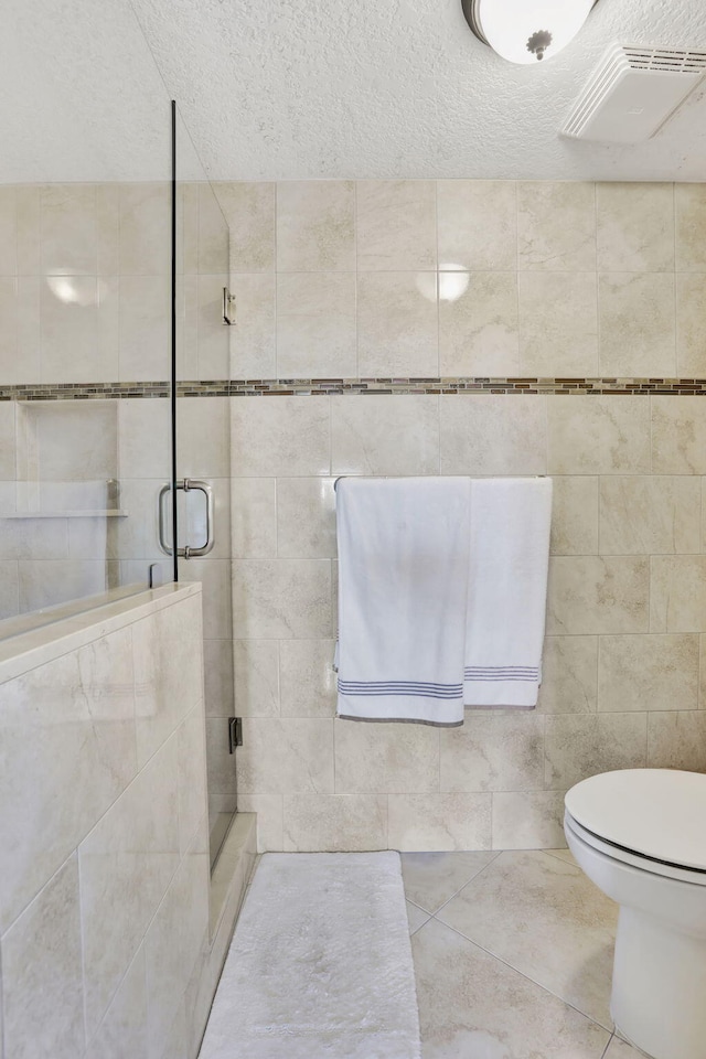 bathroom with toilet, an enclosed shower, a textured ceiling, tile walls, and tile patterned flooring