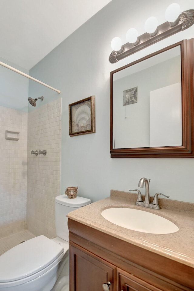 bathroom with vanity, a tile shower, and toilet