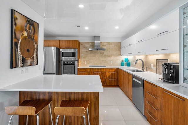 kitchen with a breakfast bar, sink, white cabinets, stainless steel appliances, and wall chimney exhaust hood