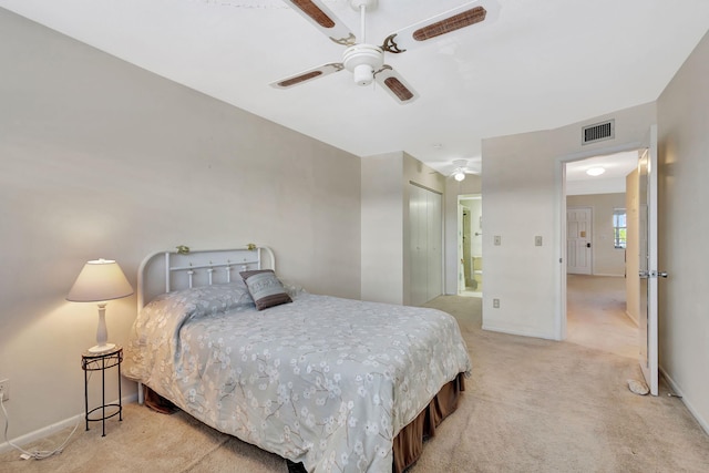 bedroom with ensuite bathroom, light carpet, ceiling fan, and a closet