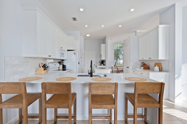 kitchen with white cabinetry, sink, a kitchen bar, kitchen peninsula, and white appliances