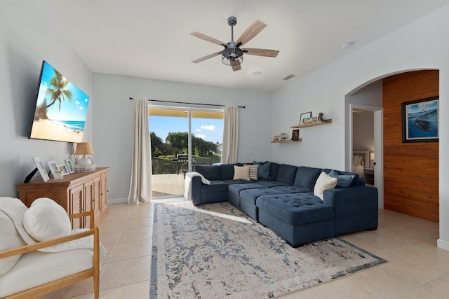 living room with light tile patterned floors, ceiling fan, and wood walls